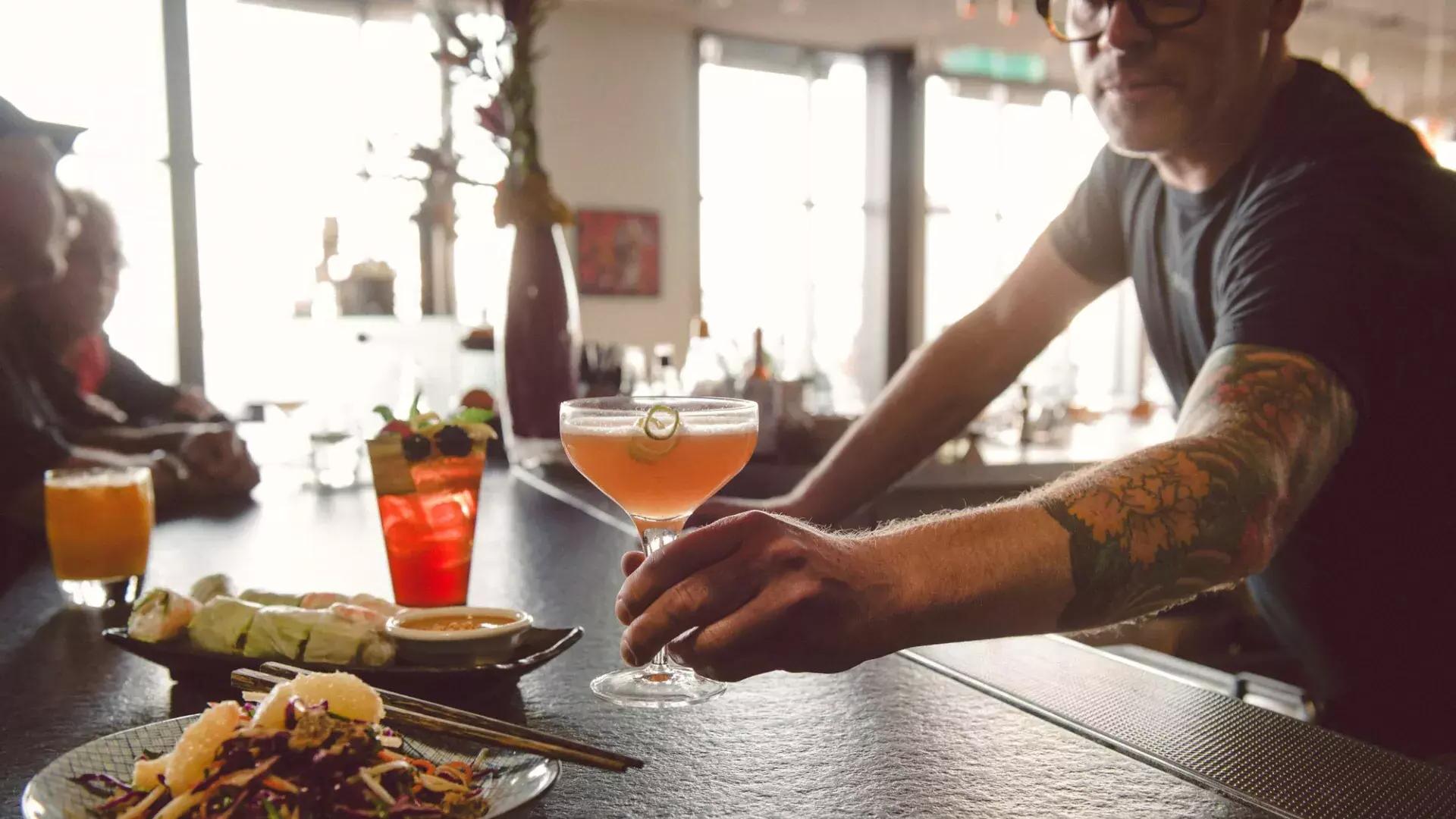 在贝博体彩app的一家酒吧，一个酒保给客人端鸡尾酒.