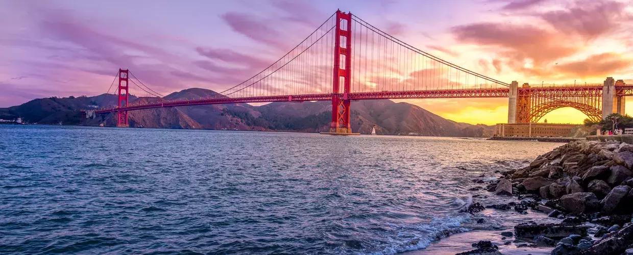 Le Golden Gate Bridge au coucher du soleil avec un ciel multicolore et la baie de San Francisco au premier plan.