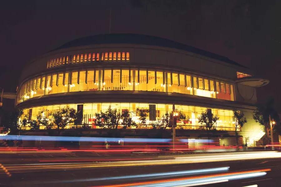 Exterior of the Louise M. Davies Symphony Hall at night with streaks of light from passing vehicles.