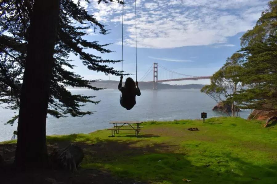 Eine Frau schaukelt auf einer Baumschaukel mit Blick auf die Golden Gate Bridge. San Francisco, Kalifornien.