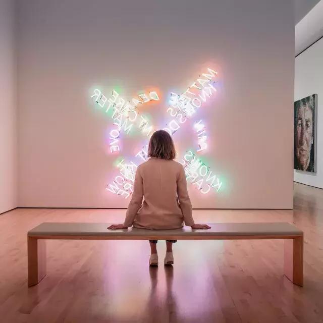 A woman, seated on a bench, looks at a piece of contemporary light art at SF MOMA in San Francisco.