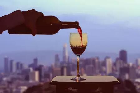 格拉斯of red wine being poured, with the San Francisco skyline可见out the window.